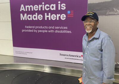 Simeon Fowler at the airport with a SourceAmerica Sign hanging on the wall behind him that says, "America is made here"