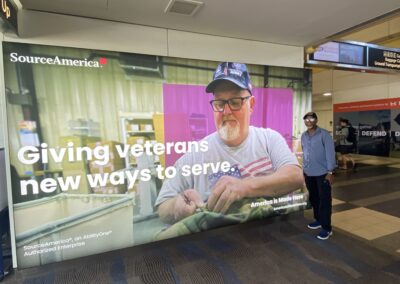 Simeon Fowler at the airport with a SourceAmerica Sign hanging on the wall behind him that says, "Giving veterans new ways to serve."