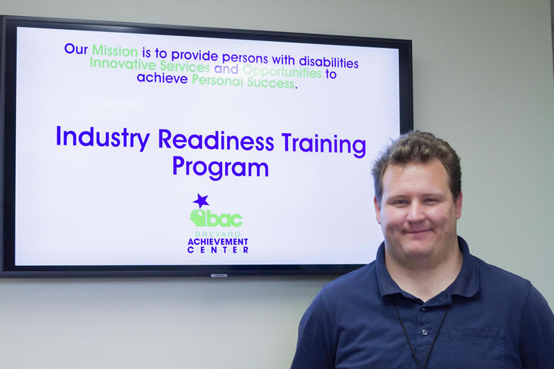Male participant posing in front of a sign for BAC's Industry Readiness Training Program