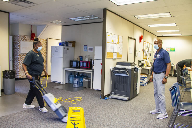 Female employee vacuuming a common area while male employee assists